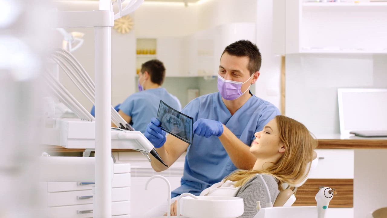 A masked Smile Makers dentist reviewing a dental X-ray with a patient in the treatment chair